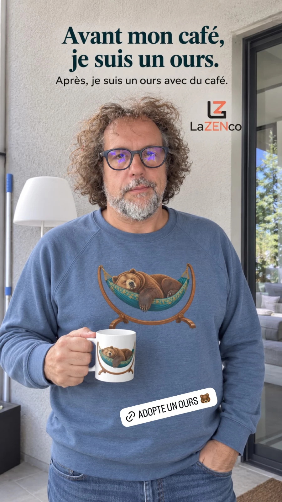 François porte un sweat bleu roi chiné et tient un mug blanc, tous deux illustrés d’un ours endormi dans un hamac fleuri.