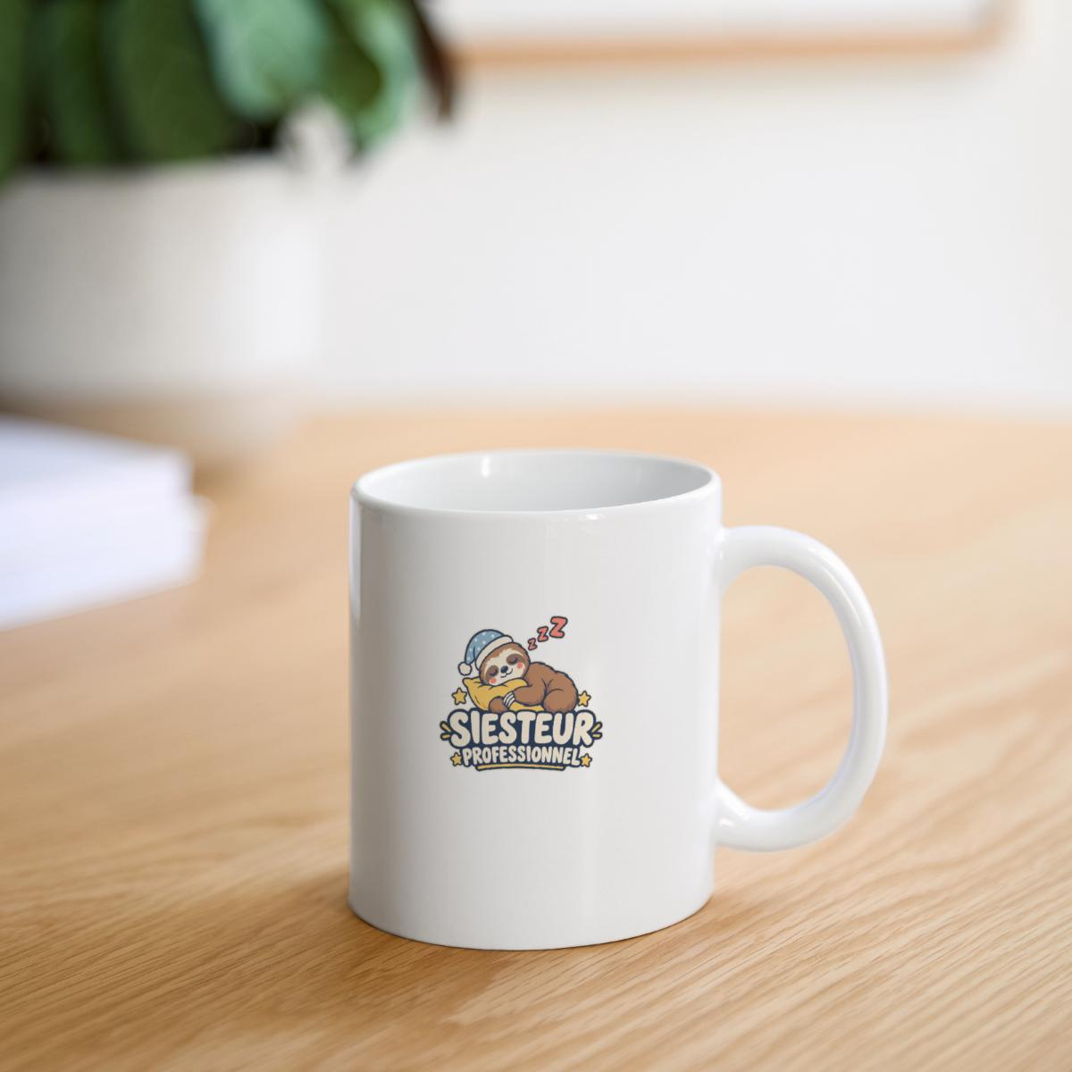 Mug blanc « Siesteur professionnel » avec un paresseux endormi, posé sur une table en bois